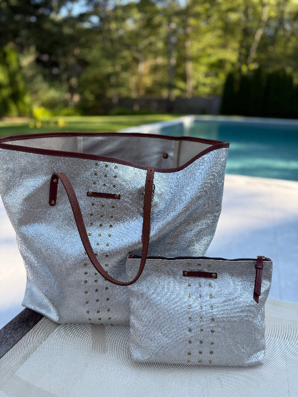 White tote bag with brown accents and a matching pouch on a table by a pool.