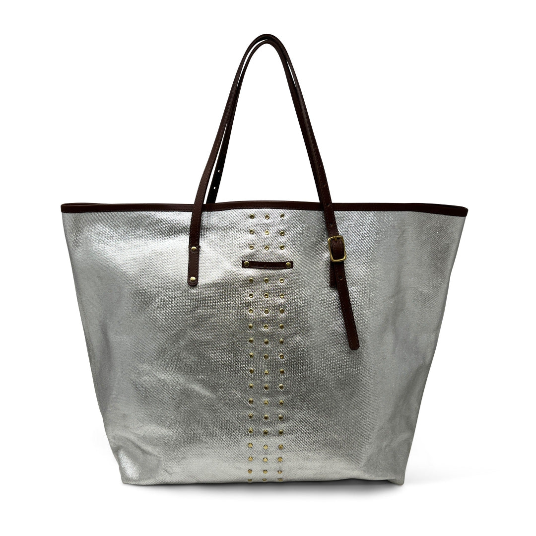 An oversized silver beach tote with metallic twill fabric, brass studding, and brown leather trim and handles.