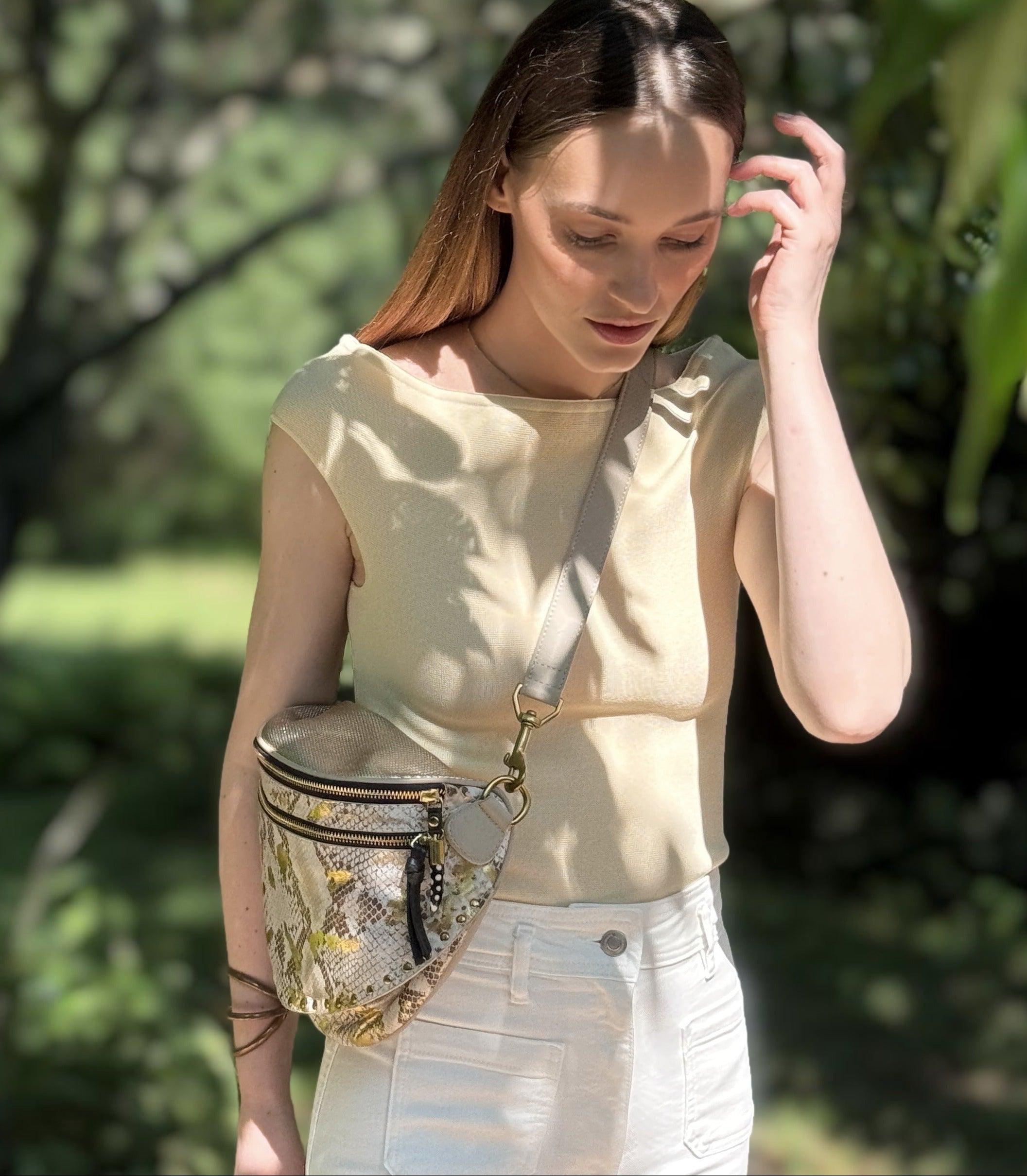 Woman wearing a beige top and white pants with a gold fanny pack in a garden setting