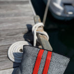 Gray textured pouch with red straps on a wooden dock with a boat in the background