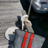 Gray textured pouch with red straps on a wooden dock with a boat in the background
