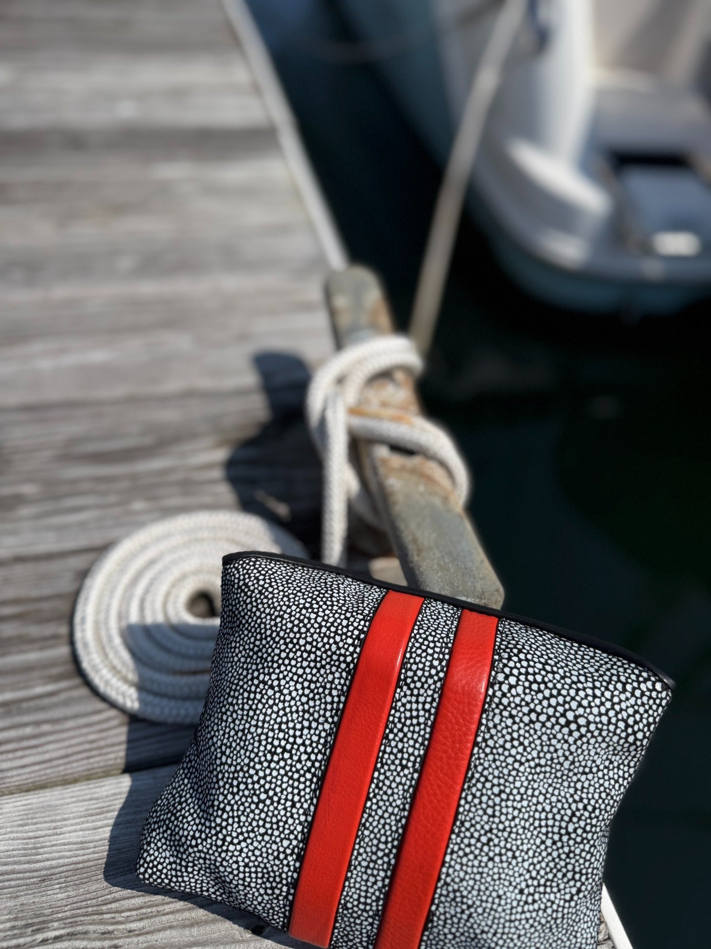 Gray textured pouch with red straps on a wooden dock with a boat in the background