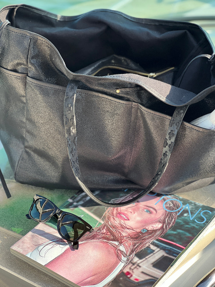 Black handbag on a surface with sunglasses and a magazine underneath