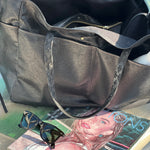 Black handbag on a surface with sunglasses and a magazine underneath
